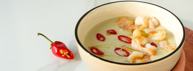 bowl of celery root soup with shrimp and chili pepper on light table