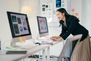 Businesswoman is analyzing marketing data on computer screen while standing in her office. She is working on her next marketing campaign