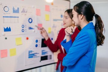Two young businesswomen discussing company data in an office, analyzing graphs and charts. Intense planning and teamwork for business success. Corporate innovation with an entrepreneurial touch