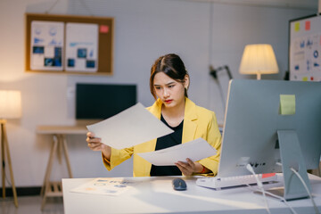 Businesswoman is sitting at her desk, reviewing documents with a serious expression on her face, suggesting she is focused and possibly facing a challenge at work