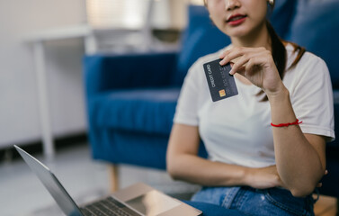 Young woman is holding a credit card while using a laptop on the floor, suggesting online shopping and e-commerce activities