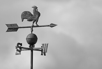 vintage metal weathervane with a rooster on top and an arrow showing the wind direction