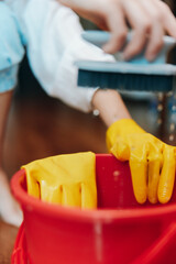 Person in yellow rubber gloves cleaning a red bucket with a brush on wooden floor in front of...
