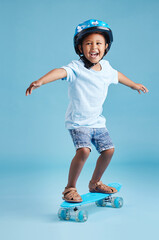 Boy, child and happy with skateboard in studio with learning, balance and excited by blue background. Kid, skater and smile with helmet for safety, games and playful with practice for development © Flashizzle/peopleimages.com