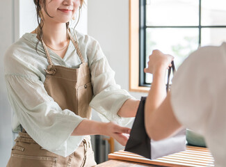カフェ・飲食店でテイクアウトの商品を客に渡す女性カフェ定員
