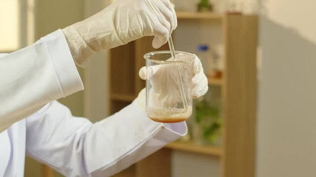 In this great close-up experiment video, a scientist is shown holding and swirling a shampoo sample in a beaker. A backdrop of a modern laboratory.