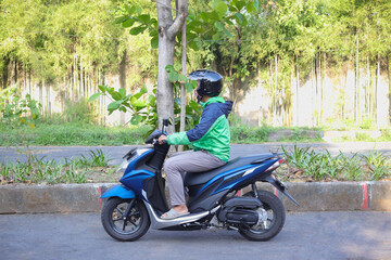 Side view of online taxi rider wearing green jacket and helmet, riding motorcycle while on the way...