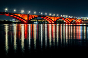 Communal bridge over the Yenisei River at night with beautiful lighting and reflection in the water