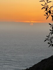 A serene coastal sunset over a misty sea, with the sun dipping below clouds on the horizon....
