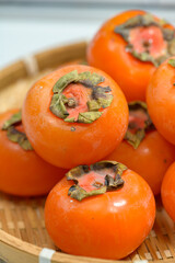 Delicious ripe persimmons in bowl on blurred background, closeup