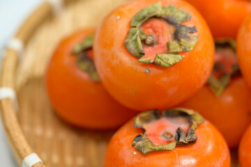 Delicious ripe persimmons in bowl on blurred background, closeup