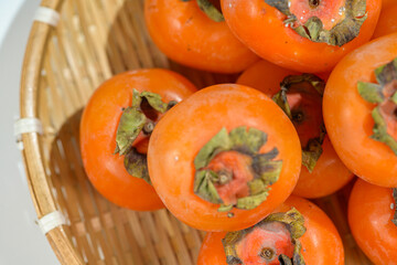 Delicious ripe persimmons in bowl on blurred background, closeup