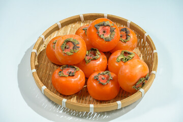 Delicious ripe persimmons in bowl on blurred background, closeup