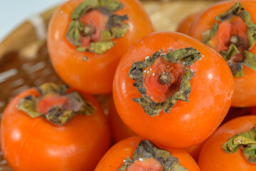Delicious ripe persimmons in bowl on blurred background, closeup