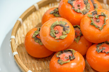 Delicious ripe persimmons in bowl on blurred background, closeup