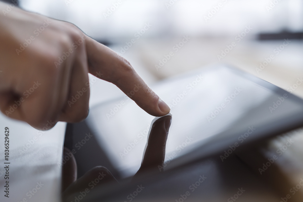 Poster Man's fingertip gently tapping the screen of a modern digital tablet lying on a desk, surrounded by the unfocused brightness of a contemporary office space