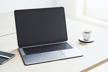 Perspective view on blank dark modern laptop screen with copyspace for your logo or text on light wooden table with coffee mug in sunny office area. 3D rendering, mockup