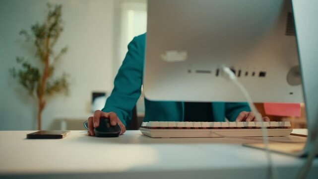 Office environment showcases a person in a suit sitting at a desk, typing rapidly on a keyboard while using a mouse, demonstrating efficiency and productivity in a corporate setting