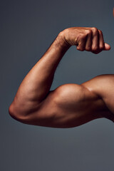 Closeup, shirtless and man with muscle, arm and flexing on gray studio background. Person, guy and...