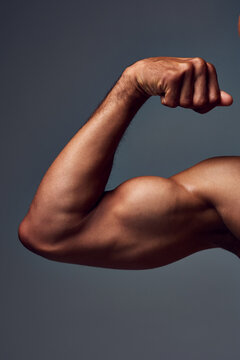 Closeup, shirtless and man with muscle, arm and flexing on gray studio background. Person, guy and model with fitness, bicep and strong with wellness, healthy and training with power and challenge