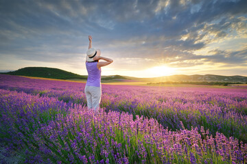 Woman in hat in meadow of lavender at sunset