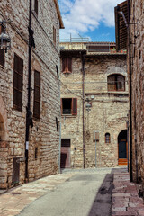 Fototapeta premium A winding alleyway in the medieval town of Assisi, Umbria, showcasing historic stone architecture under a bright sky. Assisi, Italy,