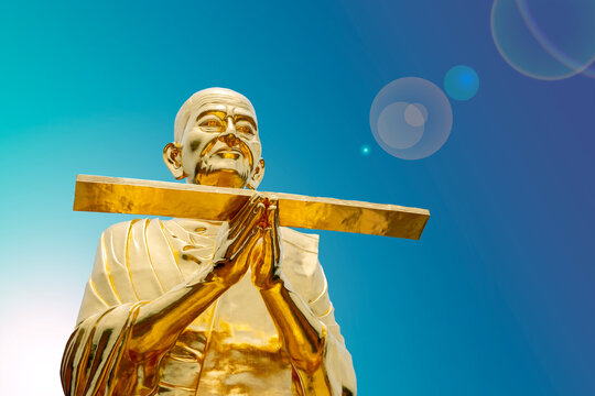 Golden monk statue with bright blue sky.