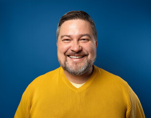 Fototapeta premium Portrait of Mature Handsome Man Happily Smiling Against Blue Studio Background