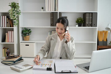 Smiling businesswoman talking on mobile phone while reviewing financial charts and graphs on the table