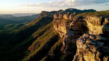 Aerial view of a dramatic cliff face with lush greenery and a sunset sky in the background.