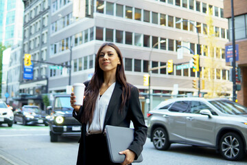 Fototapeta premium Beautiful hispanic businesswoman holding a coffee cup standing on busy city street surrounded by urban buildings