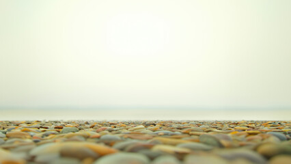 Obraz premium A serene view of smooth pebbles on a beach, blending with the gentle waves and a hazy sky in the background.