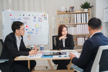 Strategic Business Meeting:  A focused team of Asian business professionals collaborates around a table, reviewing data and charts on a whiteboard and documents during a productive meeting.  
