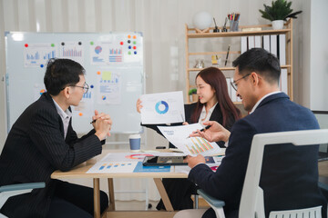 Strategic Business Meeting:  A diverse team of Asian business professionals collaborates around a table, reviewing charts and graphs during a productive meeting.