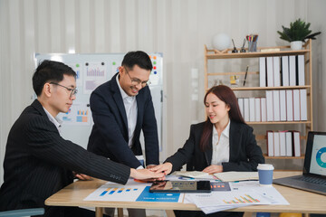 Teamwork Makes the Dream Work: A collaborative team of Asian business professionals gather around a table, hands clasped in unity, showcasing their commitment to teamwork and achieving their goals.  