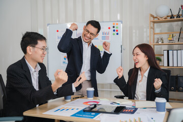 Business Success Celebration: A dynamic team of Asian business professionals rejoices in the office, celebrating a successful project or achievement. The image captures the shared excitement.
