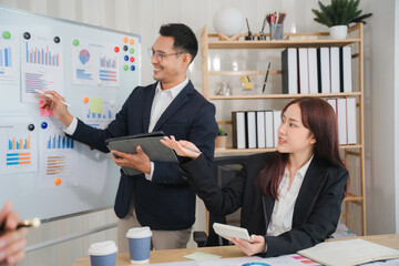 Strategic Business Presentation: A male and female business professional team collaborates during a presentation with charts and graphs on a whiteboard. The image exudes professionalism and teamwork.