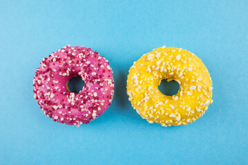 Two donuts with colored glaze and sprinkles on a blue background.