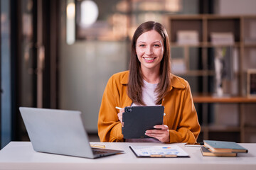 Fototapeta premium Beautiful professional woman sitting at table smiling while reading important documents with financial graphs and accounting of company.