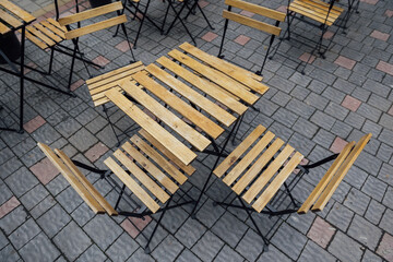 A purple colored metal patio table near a blue wooden horizontal clapboard siding exterior wall. There's a white flower pot with pink flowers on the small square table. The ground is patio flat rocks.