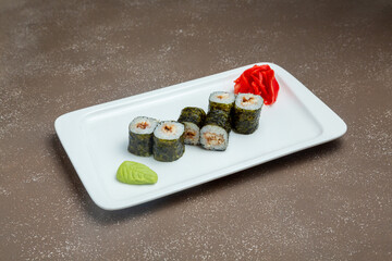 Japanese maki sushi with eel on plate with wasadi and ginger on grey background.