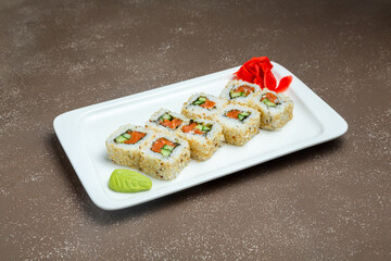Japanese rolls, sushi with red fish and cucumber, in sesame on a plate with wasabi and ginger on a gray background.