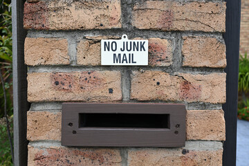 Small black and white no junk mail sign, on light brick, above the slot of a mailbox