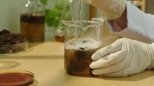 In the up-close footage, a scientist is seen stirring a solution in a beaker while surrounded by glass containers holding other herbs and test fluids.