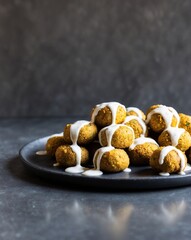 Obraz premium Golden falafel balls are drizzled with a creamy sauce on a dark counter.
