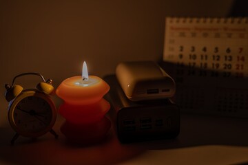 Burning candle and power banks near mechanical clock and calendar. Scheduled power outage due to...