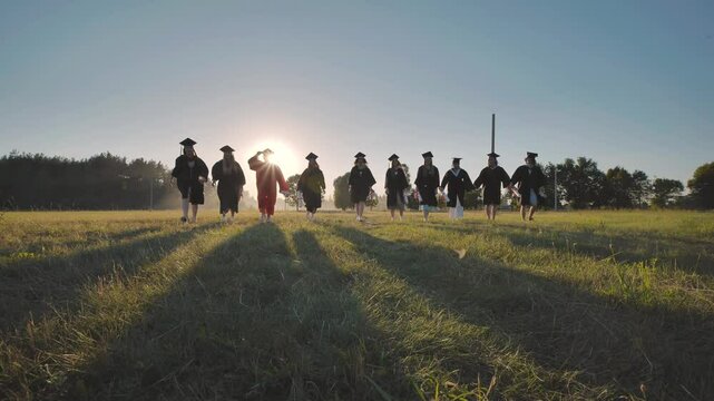 College graduates run into the sunset and throw their caps up in the air.