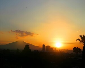 City skyline silhouette at sunset with mountain backdrop.