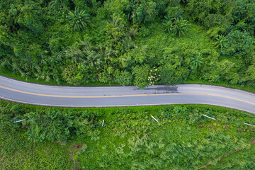 Aerial view of countryside road passing through the green forest and mountain in Thailand.