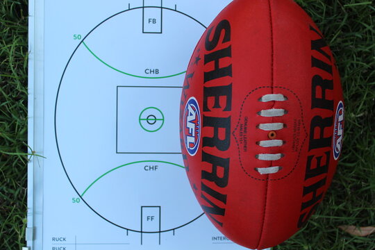 A red Sherrin AFL football on a coaches magnetic tactic board background.